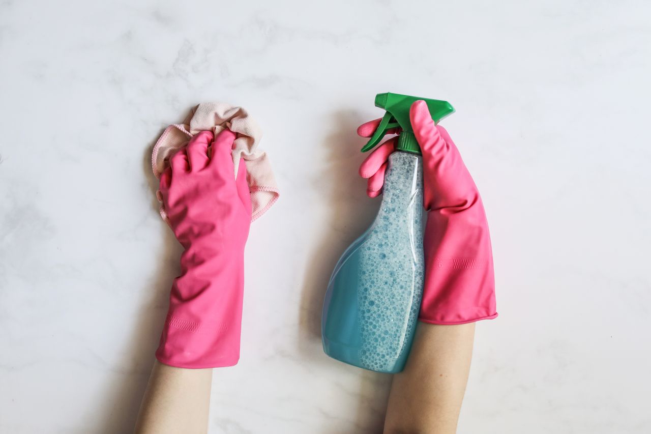heros-img A pair of hands in pink gloves are cleaning with a spray bottle on a white background.